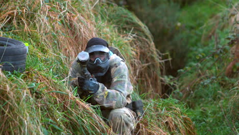 Man-kneeling-on-ground-shooting-paintball-gun