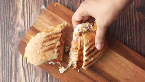 hand holding a delicious cut sandwich on a wooden board