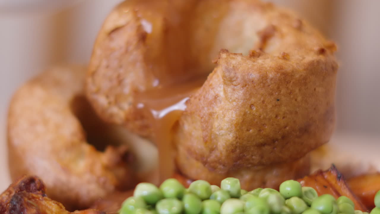Salsa che fuoriesce dallo Yorkshire Pudding al rallentatore con piselli in un classico arrosto britannico. 4K