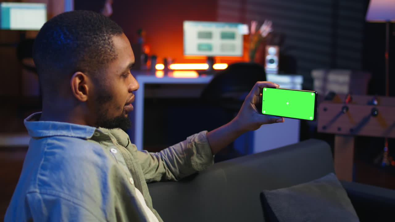 Vertical Video Black freelancer uses green screen mockup on tablet to work in the living room