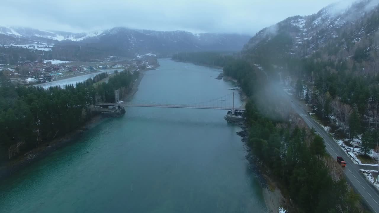 Aerial View of a Suspension Bridge Over a River in a Mountainous Winter Landscape