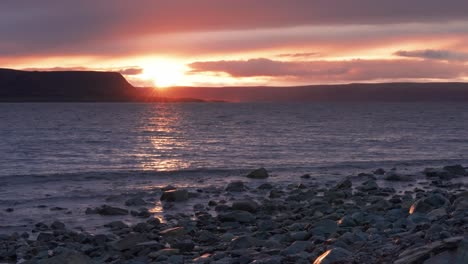 The-sun-sets-on-the-horizon,-casting-warm-light-over-the-landscape,-and-is-reflected-in-the-rippled-surface-of-the-lake-in-this-beautiful-timelapse-video