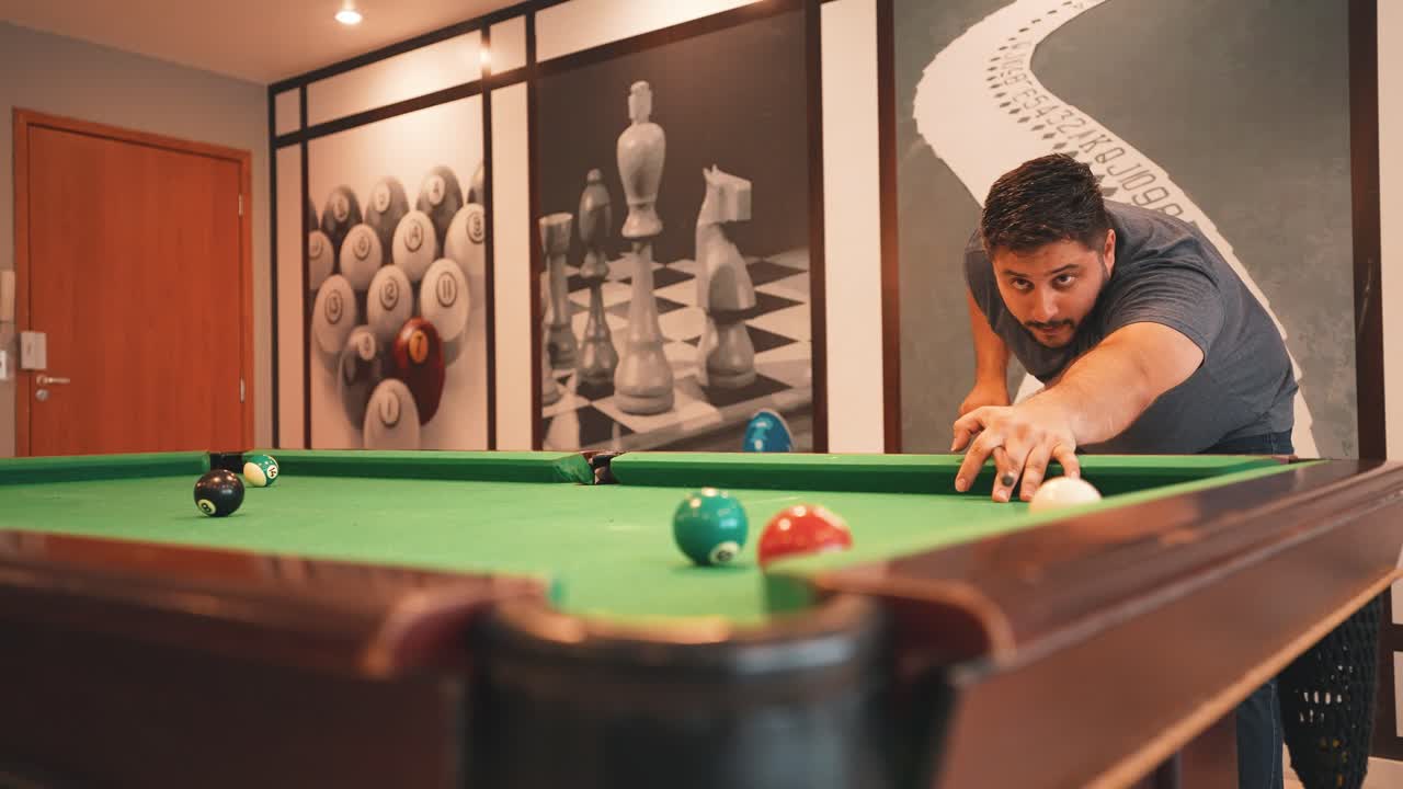 Young man sinking brown ball number seven into a pocket casual sports game of billiards on a green cloth