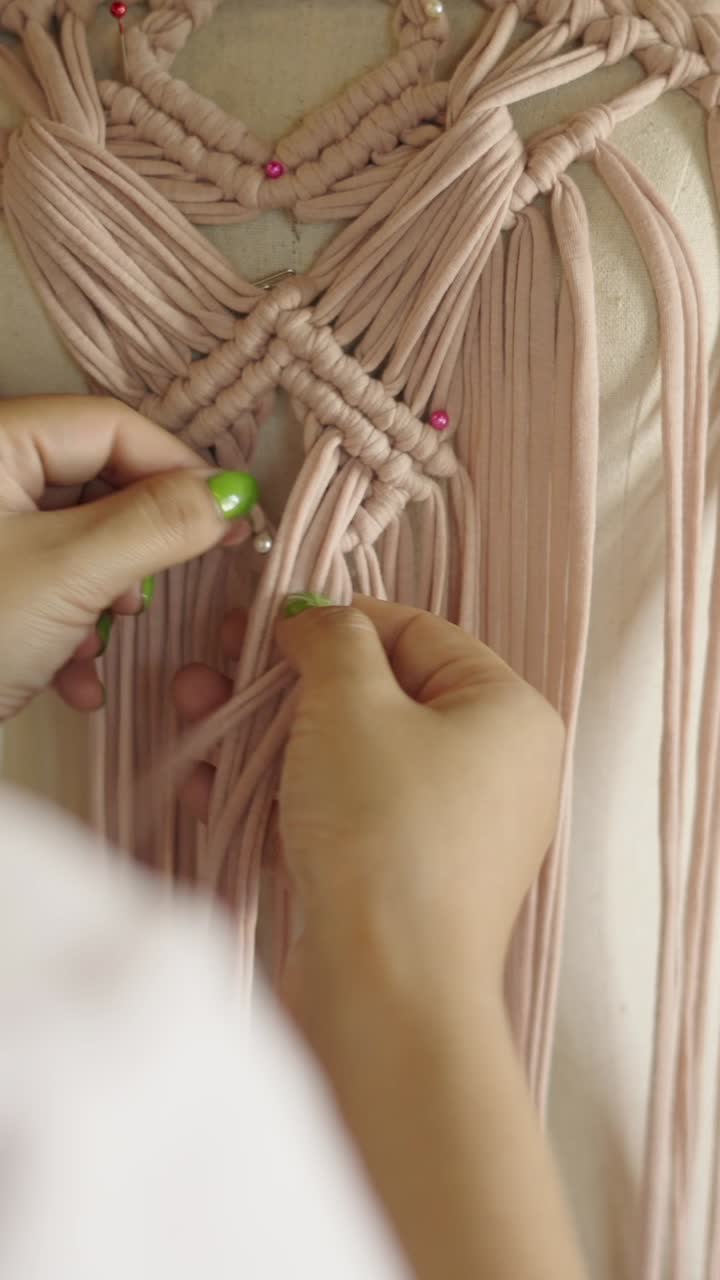 Close up of a person weaving light pink macrame