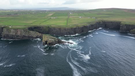 dramatic kilkee cliffs along the irish coast with lush green fields and ocean waves, aerial view