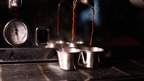slow motion view of espresso dripping from machine to fill two silver cups on grate