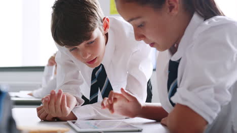 Estudiantes-Masculinos-Y-Femeninos-De-Secundaria-Vistiendo-Uniforme-Trabajando-En-Tableta-Digital-En-El-Escritorio-Juntos