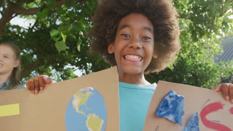 video portrait of happy african american schoolboy holding protest placards and chanting outdoors