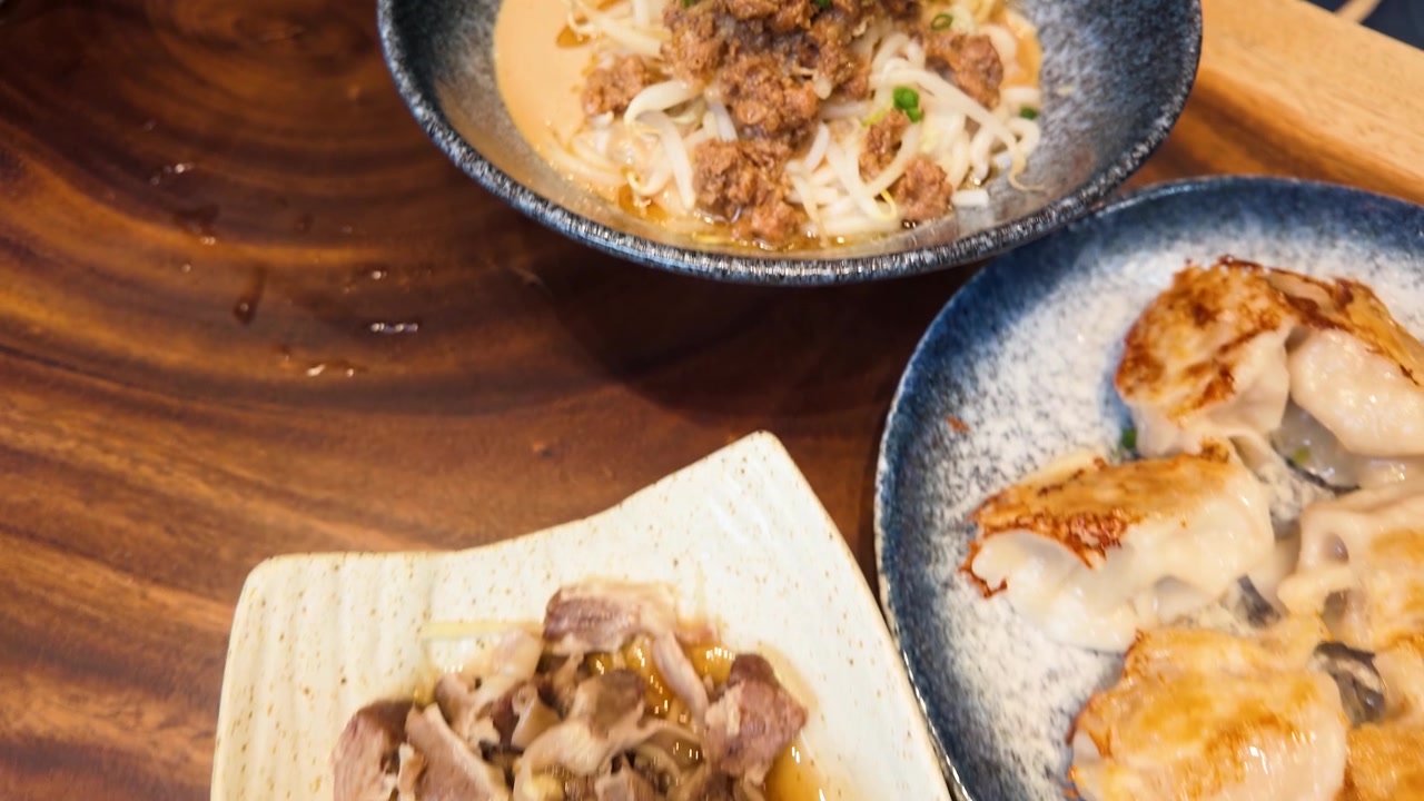 木製のテーブルに並べられた麻醤麺、餃子、スープを捉えたクローズアップのカメラパン