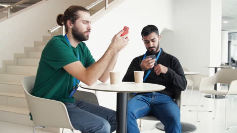 two men using smartphones at a cafe table