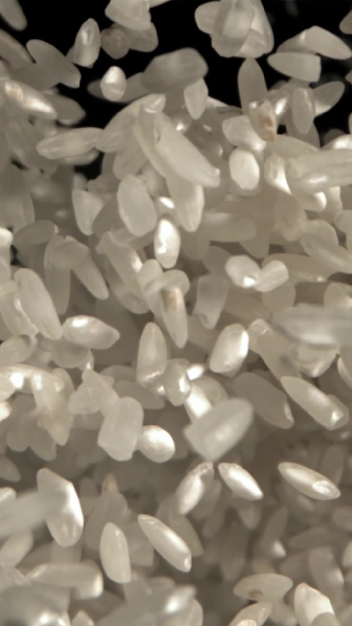 Chicchi di riso bianco che cadono al rallentatore su sfondo nero