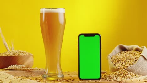 beer and smartphone on wooden table with barley