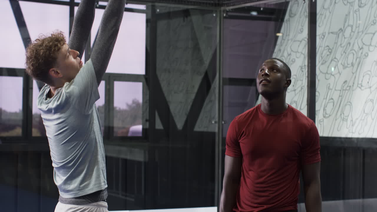 Two diverse men discussing padel tennis strategy on indoor court, holding rackets
