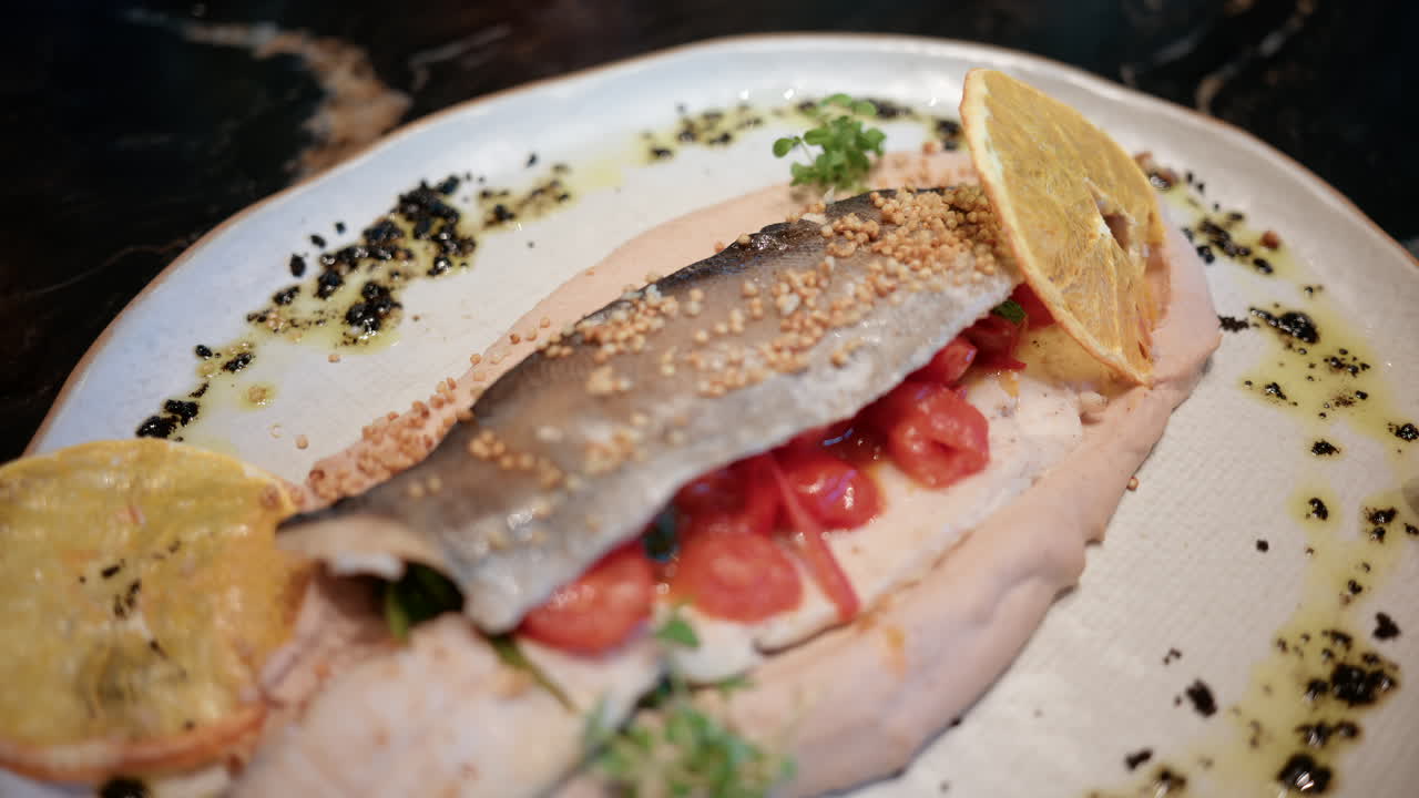 Close up of a beautifully plated fish fillet with sauce, lemon slice, and herbs