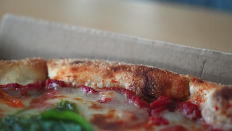 Closeup-shot-of-tasty-Neapolitan-pizza-with-pesto-sauce-in-a-cardboard-pizza-box-on-the-table,-zoom-out