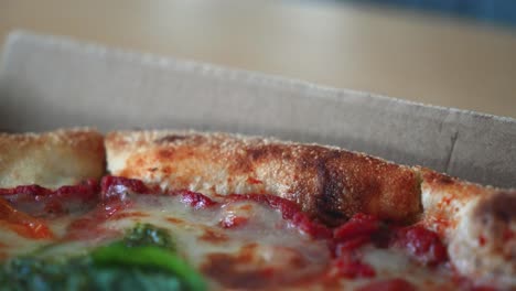 un primer plano de una sabrosa pizza napolitana con salsa de pesto en una caja de pizza de cartón en la mesa, aleja el zoom