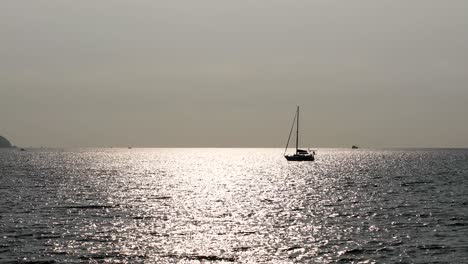 un yate aislado en el horizonte con la luz del sol reflejada en las tranquilas aguas de la costa de bangsaray cerca de pattaya, tailandia