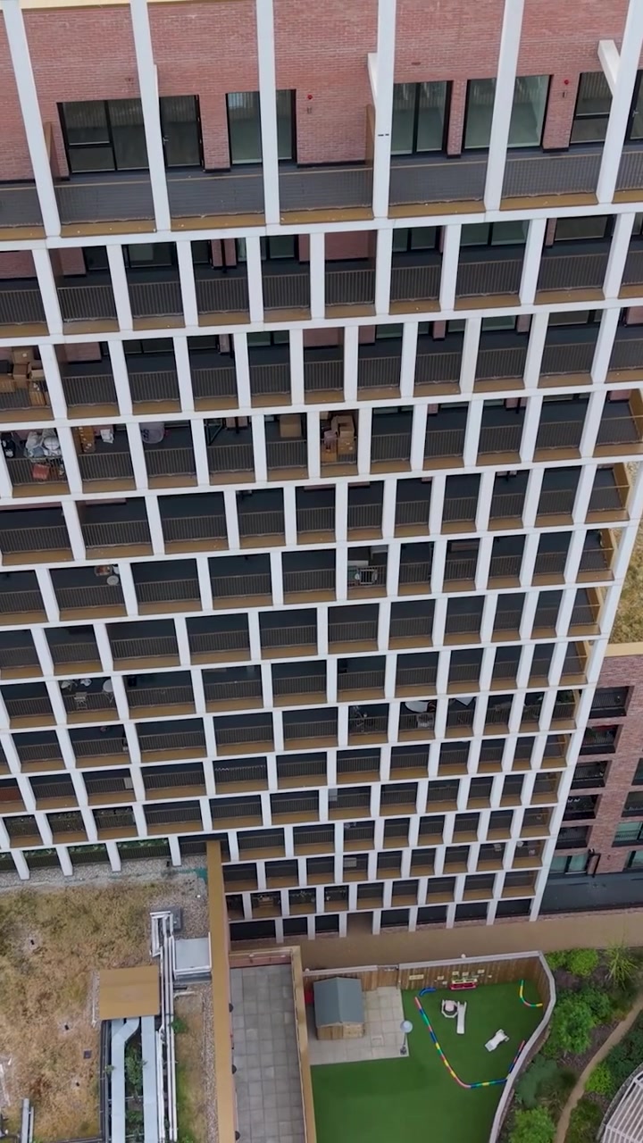 Ripresa verticale con drone in avvicinamento al grattacielo Wigeon Heights con inclinazione verso il basso da una vista frontale a una dall'alto, terminando sopra la facciata a griglia geometrica e i tetti, evidenziando l'architettura residenziale moderna