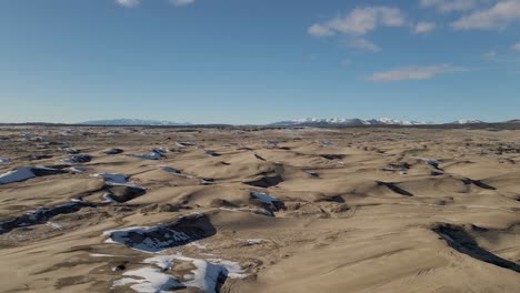 low angle aerial pan shot of little sahara sand dunes covered with snow and ice during sunny day and blue sky in winter