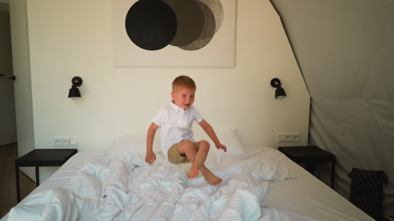 사랑스러운 유아는 편안한 침대에 뛰어다니며 재미를 느니다. 금발 아이는 밝은 방에서 놀면서 기을 발산합니다. 흥미진진한 순간으로 가득 찬 행복한 어린 시절 기억