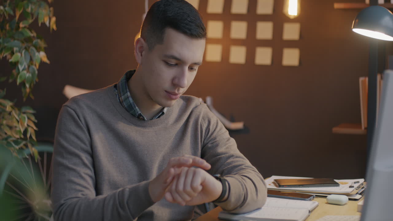 Young man working from home/office checking time on smartwatch.