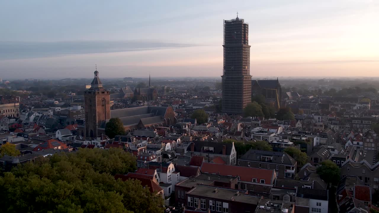 Domkirketårnet De Dom fra middelalderen i stillads og Museum Speelklok ved solopgang i Utrecht centrum, der tårner sig op over bybilledet med udsigt mod Hovedbanegården Hoog Catharijne.