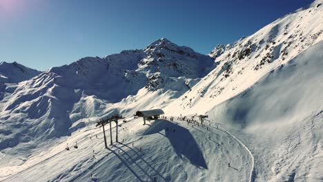 Chairlift-end-station-with-skiers-high-in-Alps-during-winter-season,-aerial