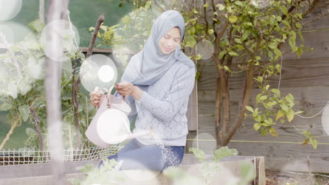 animation of spots of light over biracial woman in hijab with watering can, gardening