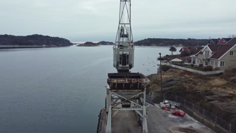 old rusty harbor crane in lillesand norway - aerial rotating around crane wit grab and north sea in background