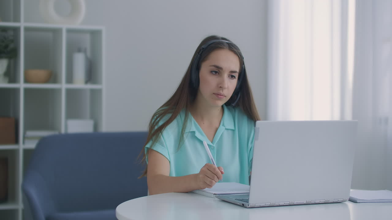 mujer estudiante sentarse en el escritorio en casa usar auriculares hablar a distancia por video llamada aplicación y dispositivo portátil e-aprender idiomas estudiar con e tutor o compañero de clase hacer tarea común remotamente concepto de tecnología moderna