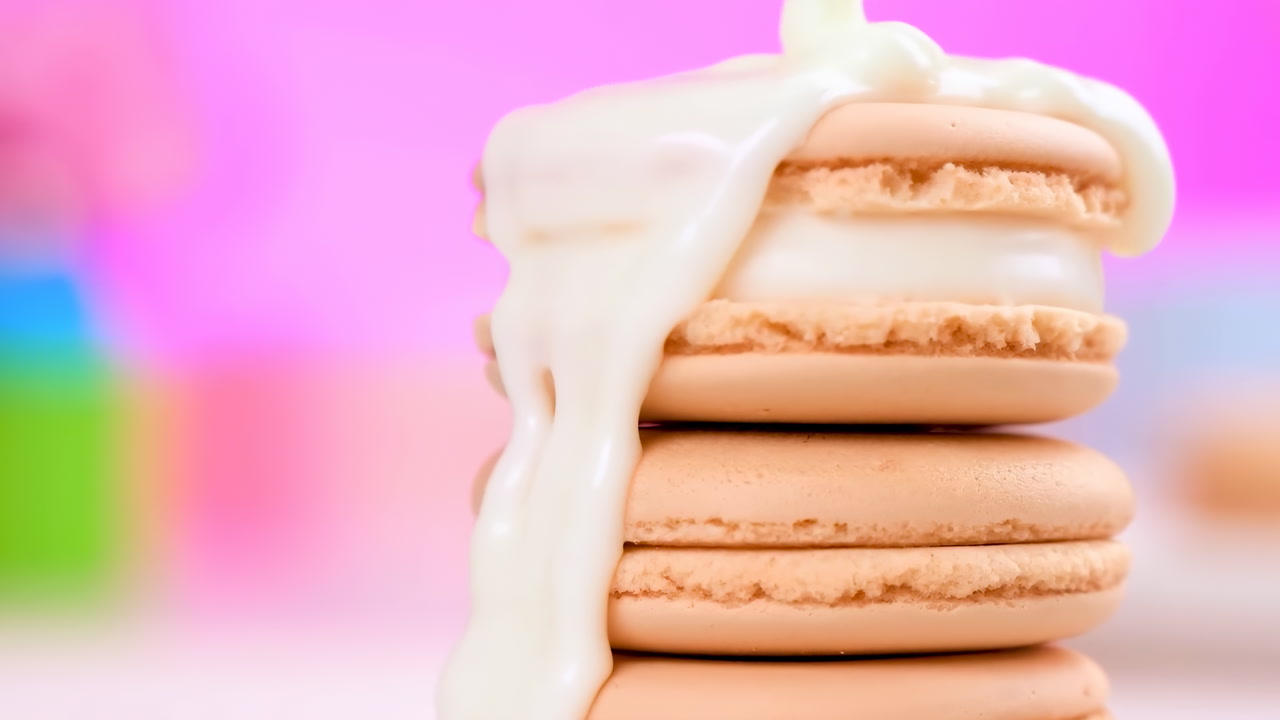 Stacked Beige Macarons With Drizzle And Glossy Cream Cascading Over Three Delicate Cookies On Pastel Pink