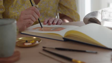 close up of woman painting a face with paintbrush in notebook