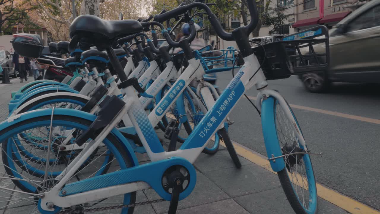 A row of neatly placed shared bicycles on a busy street in Shanghai waiting for people to scan them. Alipay brand Hello Bike.