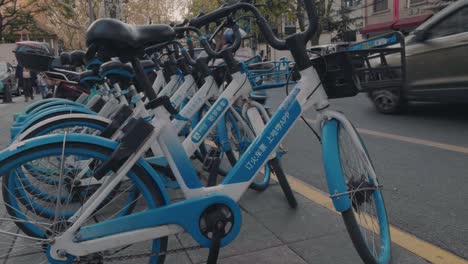 a row of neatly placed shared bicycles on a busy street in shanghai waiting for people to scan them. alipay brand hello bike.