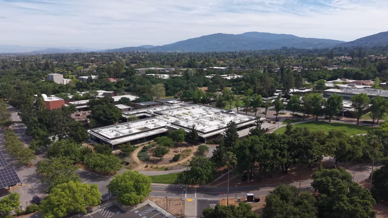 Vista panorámica giratoria de dron del campus de West Valley College, ubicado en la ciudad de Saratoga, California, con las montañas de Santa Cruz visibles en el pintoresco fondo en un día parcialmente nublado.
