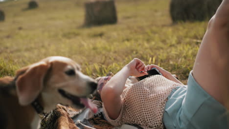 tourist in net cloth and sunglasses lying on mat with warm smile observing her hand as dog on leash stands close, serene countryside setting, peaceful relaxation