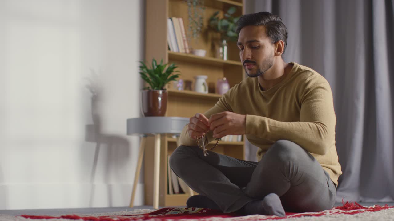 Muslim Man Praying Holding Prayer Beads Sitting On Floor At Home