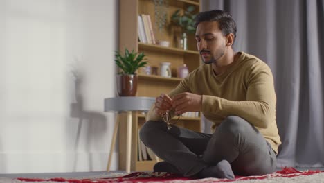 muslim man praying holding prayer beads sitting on floor at home