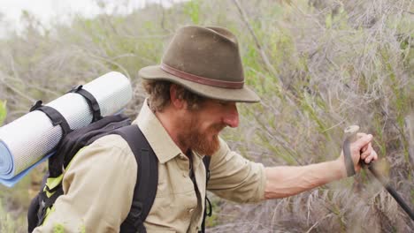 un survivalista caucásico sonriente caminando por el desierto con mochila y palos para caminar