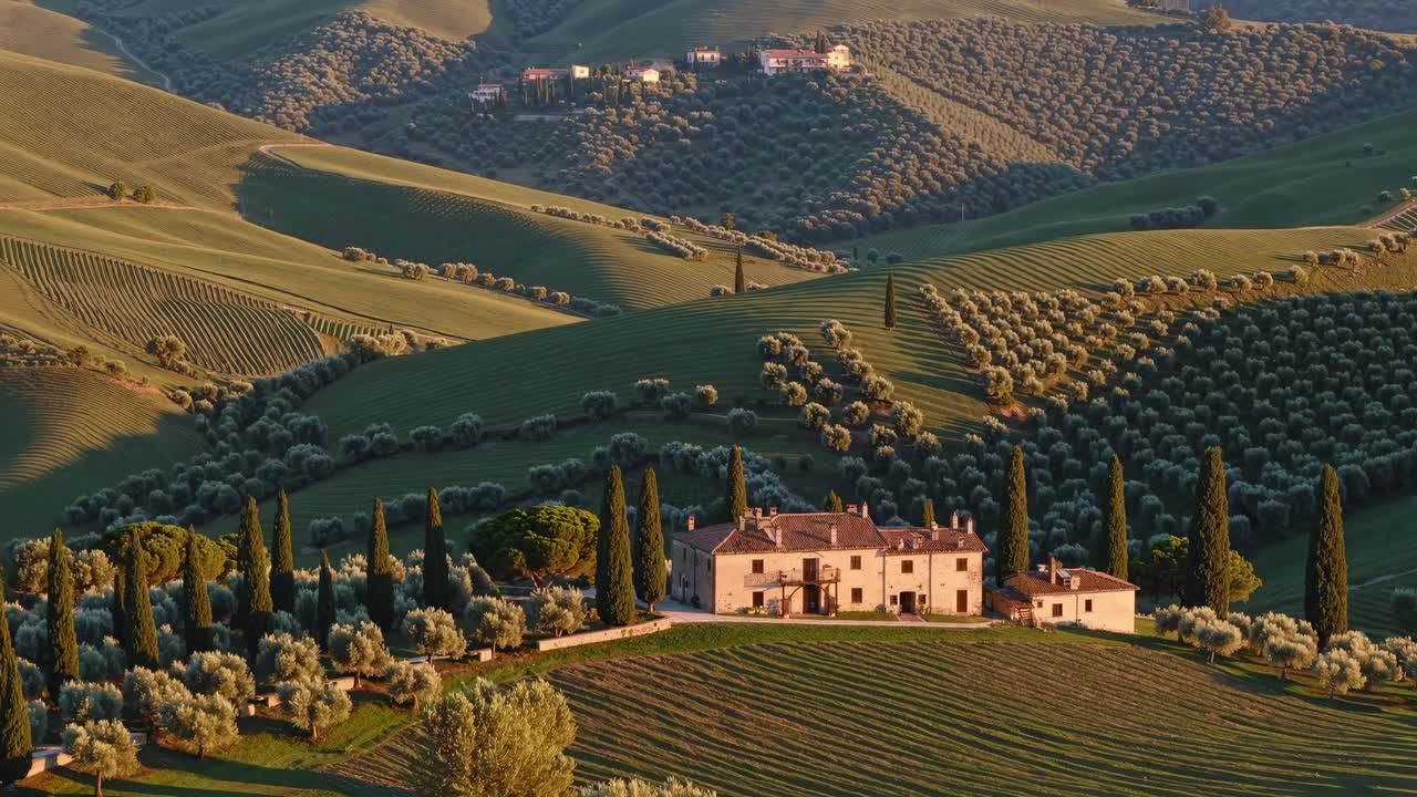 Vue aérienne d’une villa rustique au milieu de collines ondoyantes et d’oliveraies, capturant le paysage serein