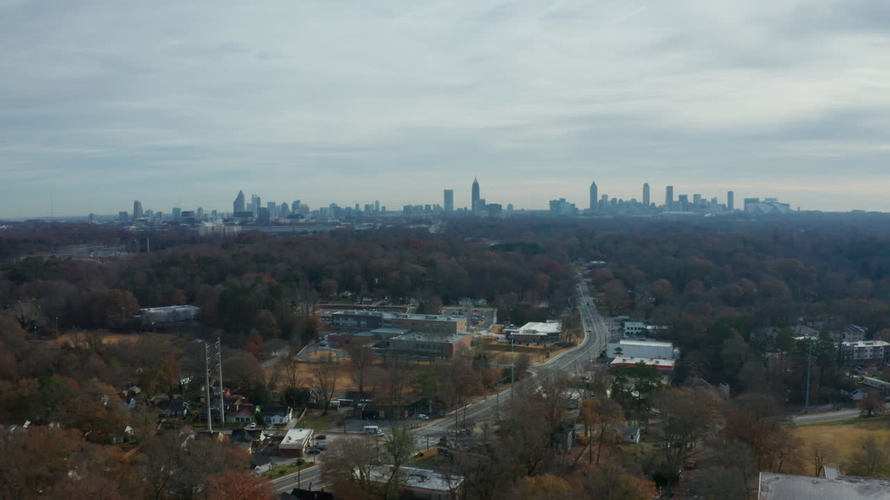 A scenic aerial over the tree canopy surrounding the suburbs of Atlanta, with a busy road and drivers coming to and from the city, with the skyline in the background cityscape.