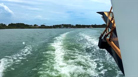 Looking-out-to-the-stern-of-a-car-ferry-traversing-the-choppy-waters-of-Queensland's-Moreton-Bay,-as-the-Australian-coast-at-Cleveland-can-be-seen-in-the-background-and-the-sea-is-churned-to-foam