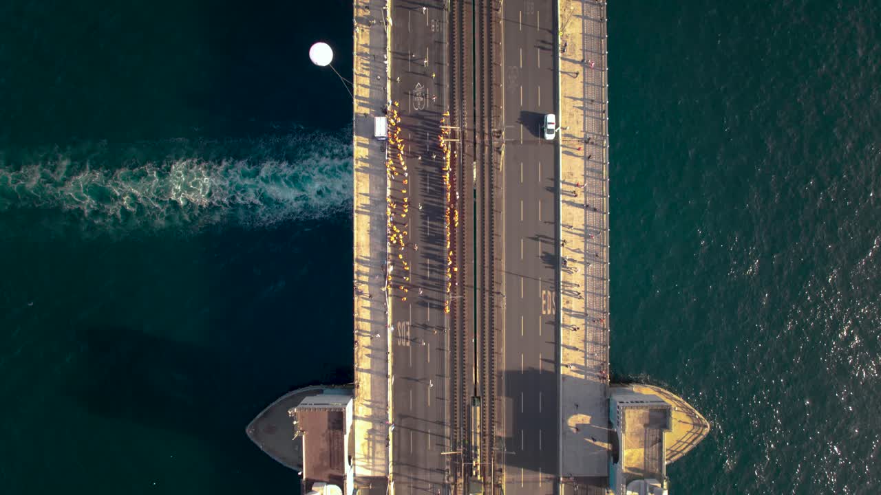 Top-view drone shot tracking Istanbul Marathon runners across Galata Bridge. Ideal for sports coverage, aerial documentaries, marathon promos, and dynamic city footage