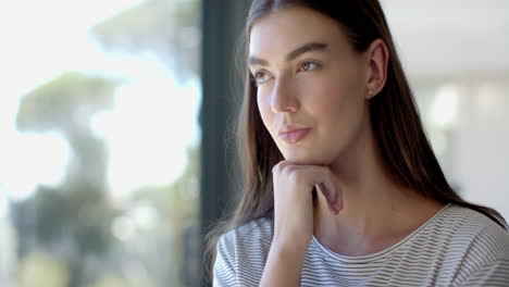 Teenage-Caucasian-girl-with-long-brown-hair-ponders-by-a-large-window-at-home