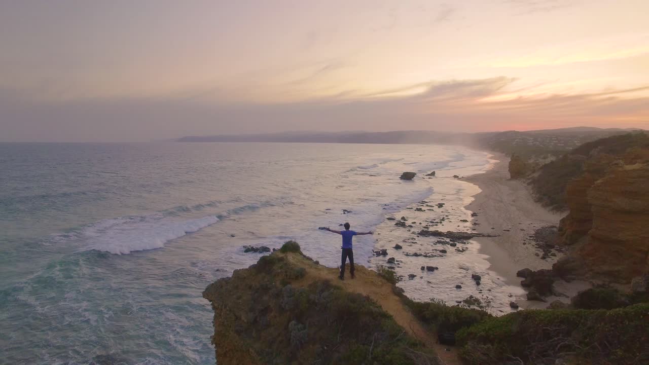 Great Ocean Road in Australia Cape Otway Lighthouse - Lightstation. Model holding up hands in celebration on road trip on cliff edge.  4K drone at sunset.