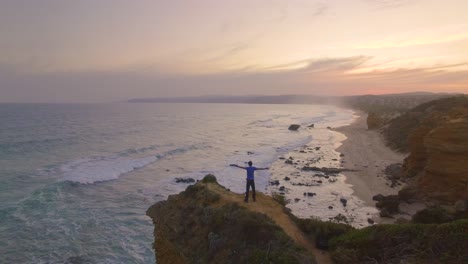 great ocean road in australia cape otway lighthouse - lightstation. model holding up hands in celebration on road trip on cliff edge.  4k drone at sunset.