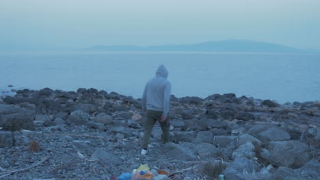 Male-youth-throws-plastic-on-seaside-shoreline-from-pocket