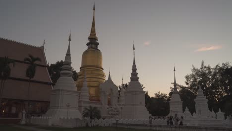 golden pagoda and white stupas at a thai temple at sunset