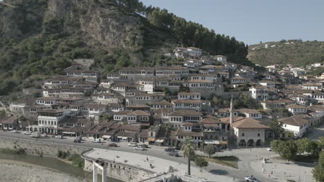 Drone-shot-of-the-city-of-Berat-and-its-castle-and-fortress-in-Albania,-the-city-of-a-thousand-windows-on-a-sunny-day-in-the-valley-with-blue-sky-with-white-houses-near-the-mountains-LOG