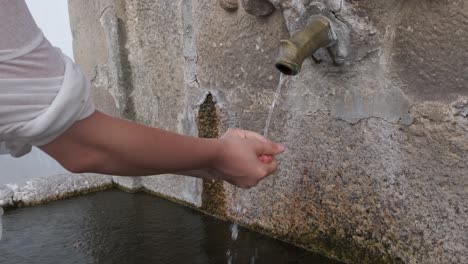 Unrecognizable-woman-washes-hands-in-fountain-of-Monsanto-village